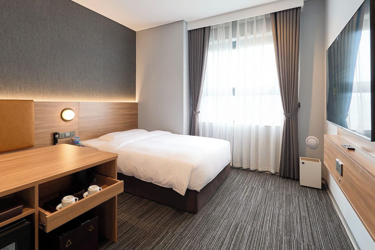 Una habitación de hotel con una cama, un escritorio, un televisor y una ventana con cortinas.