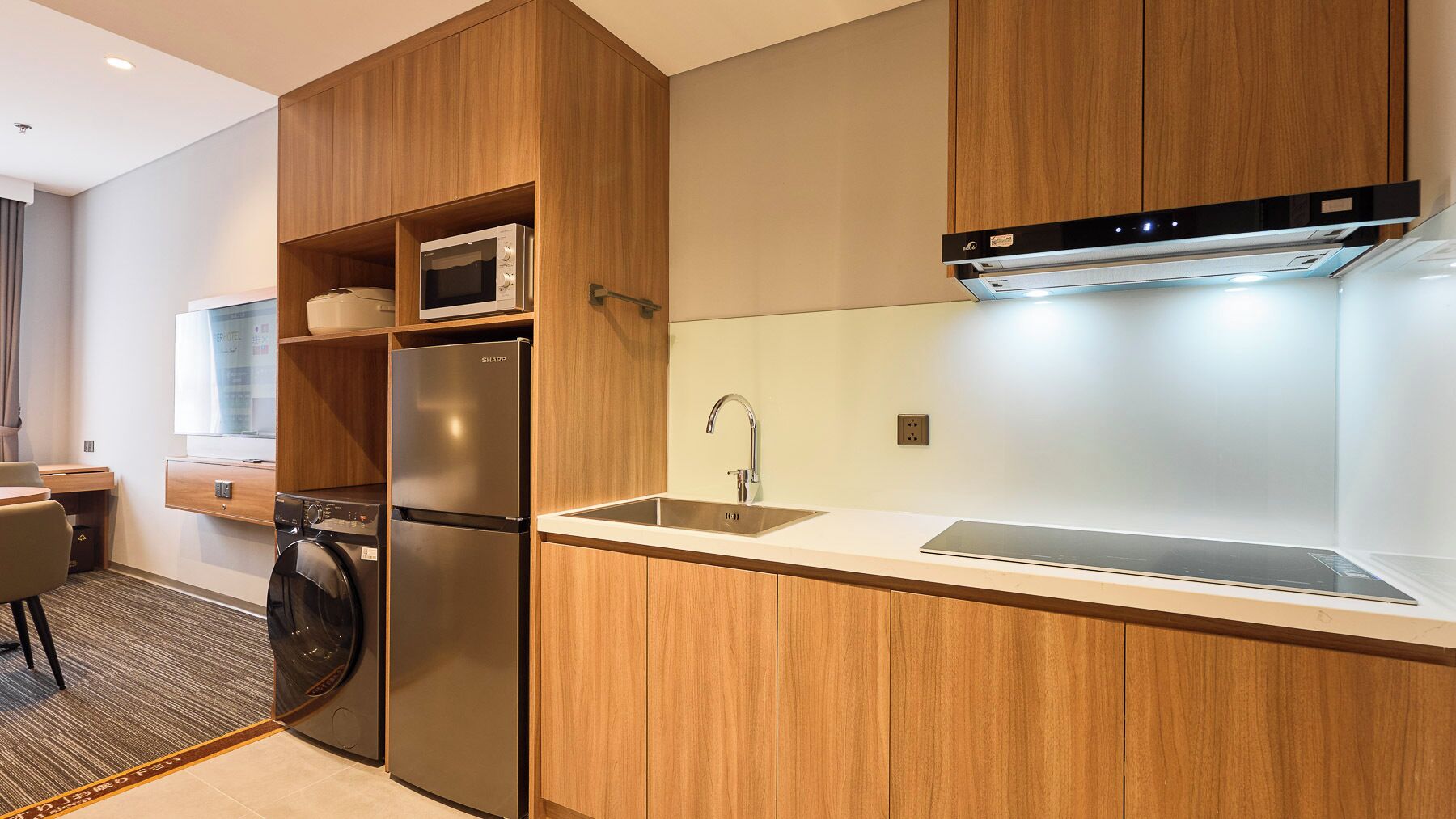 Una cocina moderna con armarios de madera, microondas integrado, refrigerador de acero inoxidable, un lavaplatos y lavavajillas.