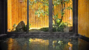 Un intérieur japonais traditionnel avec un mur en bambou, un jardin de rochers et une surface d’eau qui reflète la lumière.