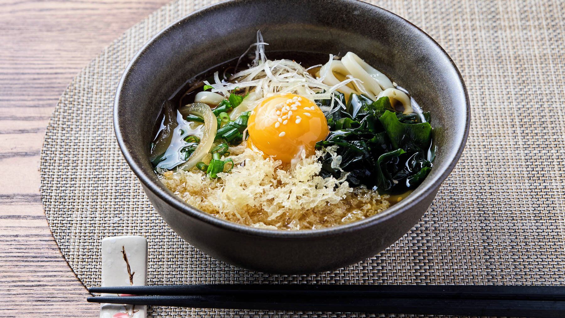 Un tazón de ramen con huevo, alga marina y fideos sobre un tapete tejido.