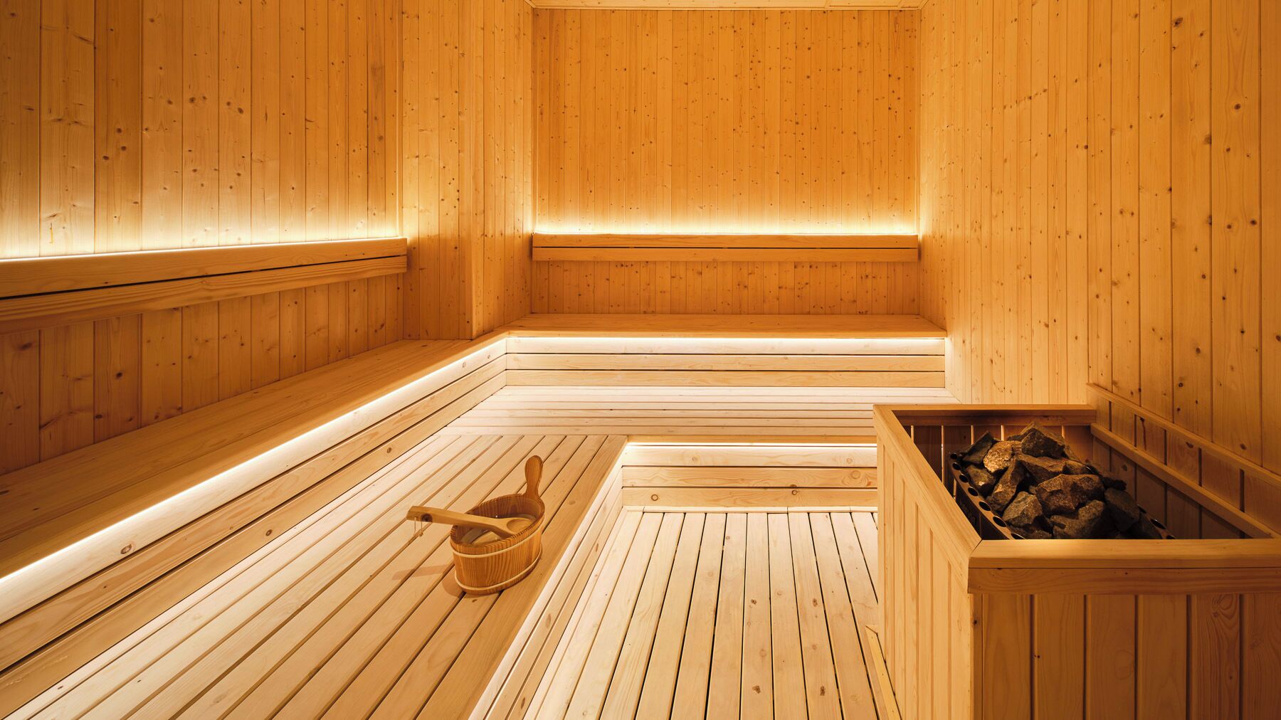 Uma sauna de madeira com bancos, piso de madeira e um balde.