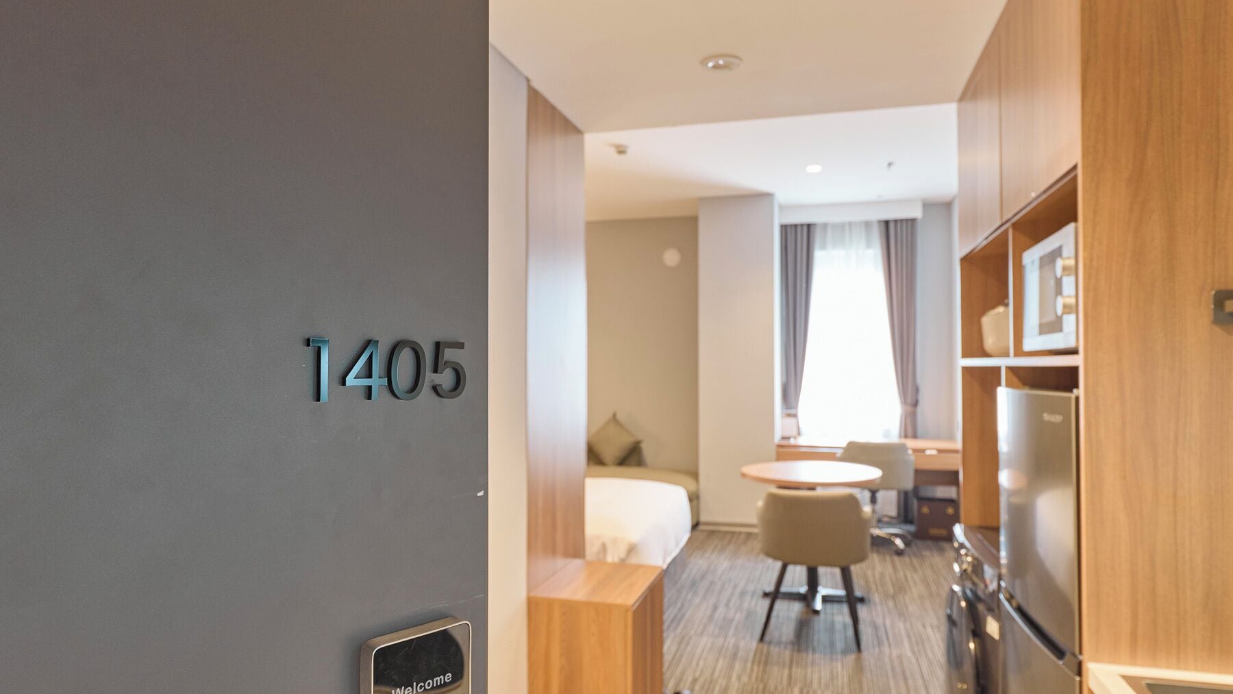 A hotel room with a bed, a desk, a chair, a small table, and a refrigerator.