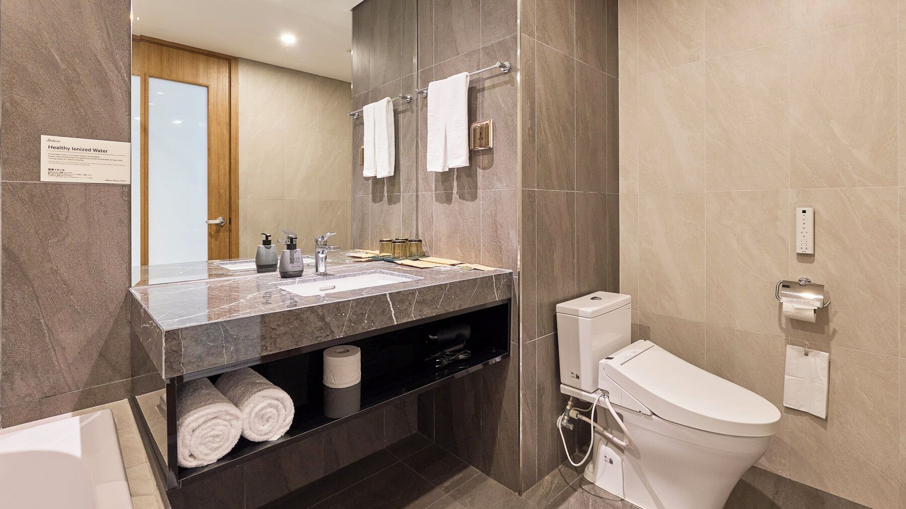A modern bathroom with a marble countertop, a toilet, and a large mirror.