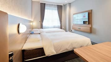 Una habitación de hotel con dos camas, televisión, escritorio y ventana con cortinas.