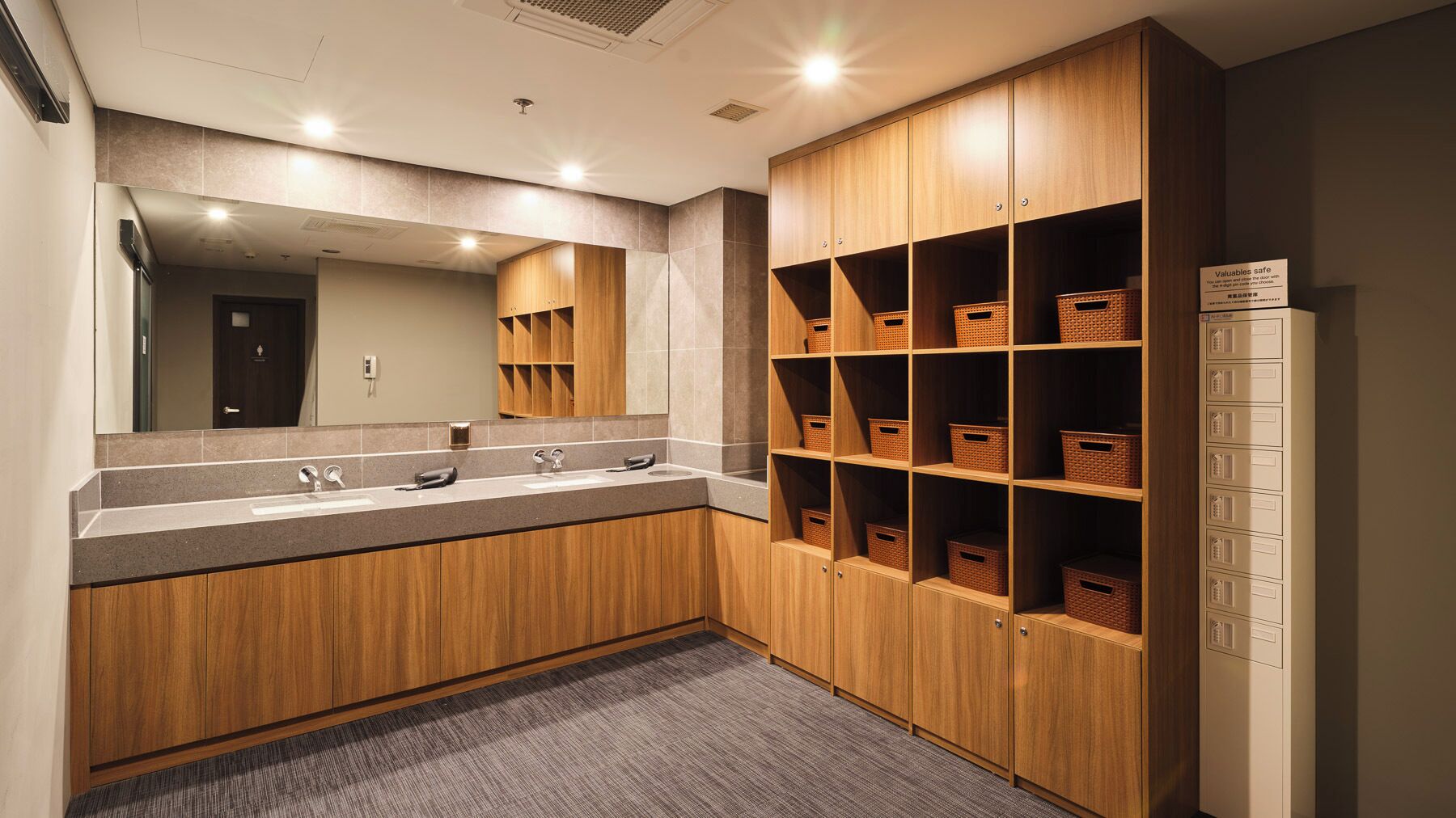 A modern bathroom with wooden cabinets, a large mirror, and storage baskets.