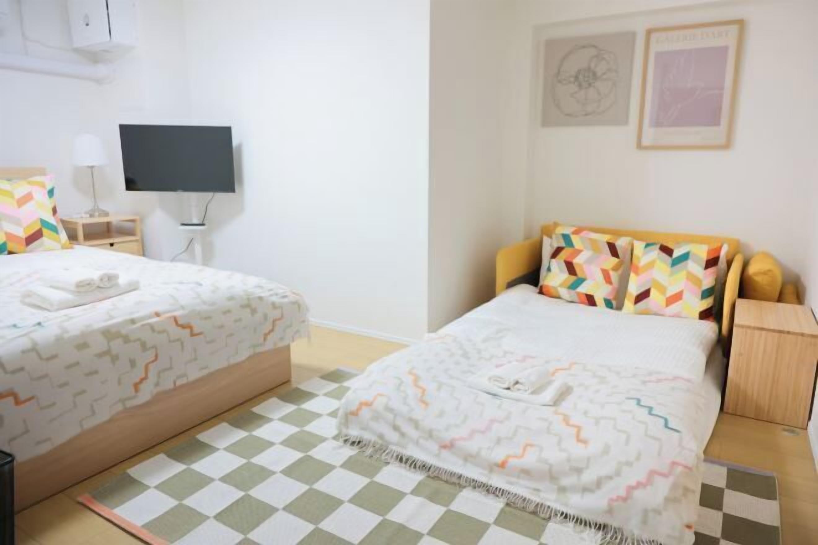 A hotel room with two beds, a TV, a checkered floor, and artwork on the walls.