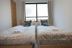 Una habitación con dos camas, una ventana con cortinas y una puerta de madera.
