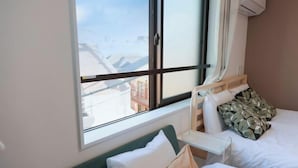 Une chambre d’hôtel comprenant un lit, une table de chevet, une fenêtre donnant sur des immeubles et un climatiseur fixé au mur.