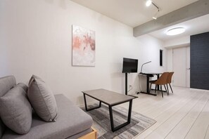 A modern living room with a sofa, a coffee table, a TV, and a dining area. - Blossom Terrace Ryogoku (Tokyo)