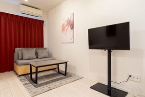 A room with a sofa, a coffee table, a flat-screen TV, and a red curtain. - Blossom Terrace Ryogoku (Tokyo)