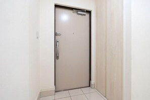 Een gesloten deur met een handvat, een klein raam erboven en een lichtschakelaar aan de muur.