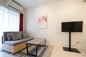 A modern living room with a sofa, a coffee table, and a flat-screen TV mounted on the wall. - Blossom Terrace Ryogoku (Tokyo)