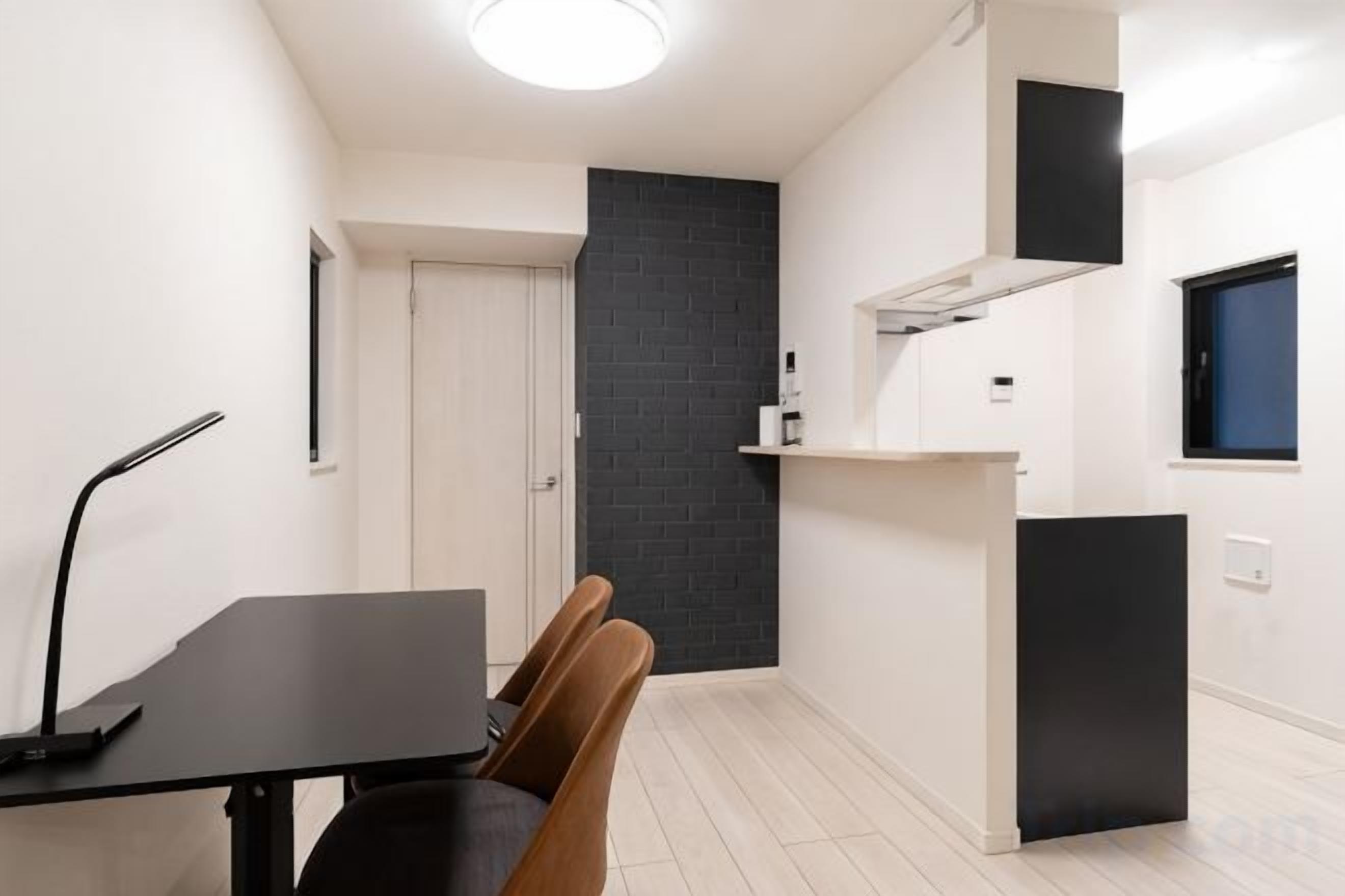 Una habitación compacta con una mesa de comedor, sillas, un armario negro y una pared oscura.