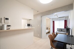 A modern kitchen with a microwave, a coffee maker, and a small refrigerator. There is a dining area with a table and chairs. - Blossom Terrace Ryogoku (Tokyo)