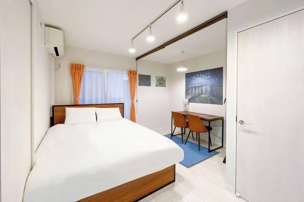 Habitación de hotel con cama, escritorio con silla, ventana con cortinas y un cuadro en la pared.