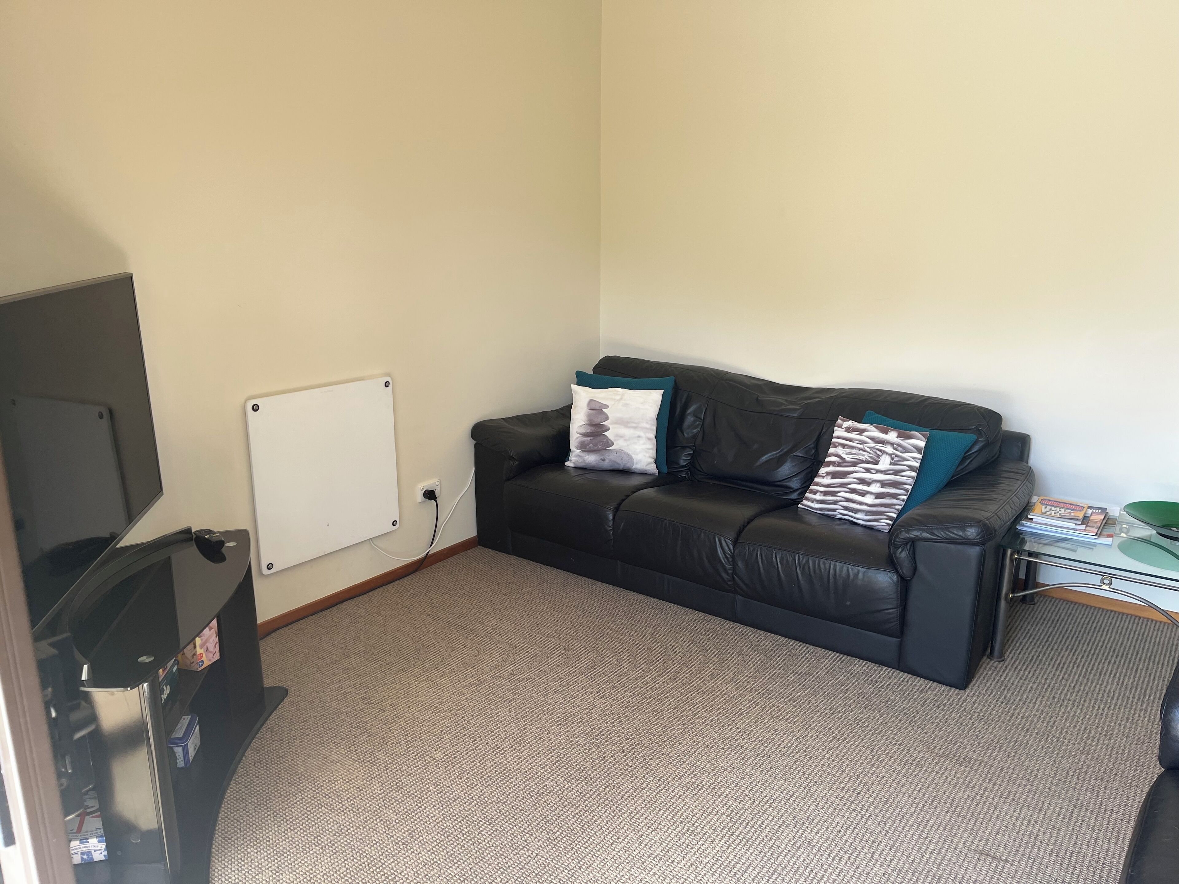 A living room with a black leather sofa, a whiteboard, and a television.