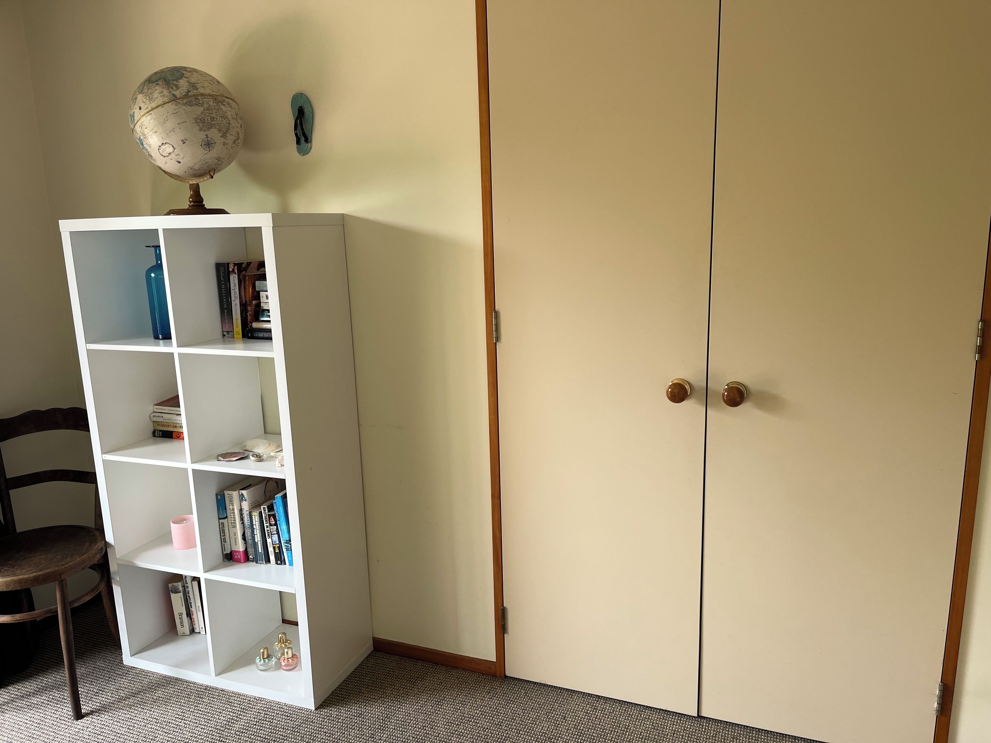 Une pièce avec une bibliothèque blanche, un globe terrestre, une paire de chaussons et une armoire à deux portes.