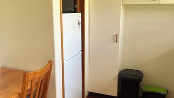 Une petite cuisine équipée d’un réfrigérateur, d’une chaise en bois, d’une poubelle et d’un placard.