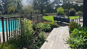 Un jardin avec une terrasse en bois, une piscine et un espace patio aménagé avec du mobilier d’extérieur.