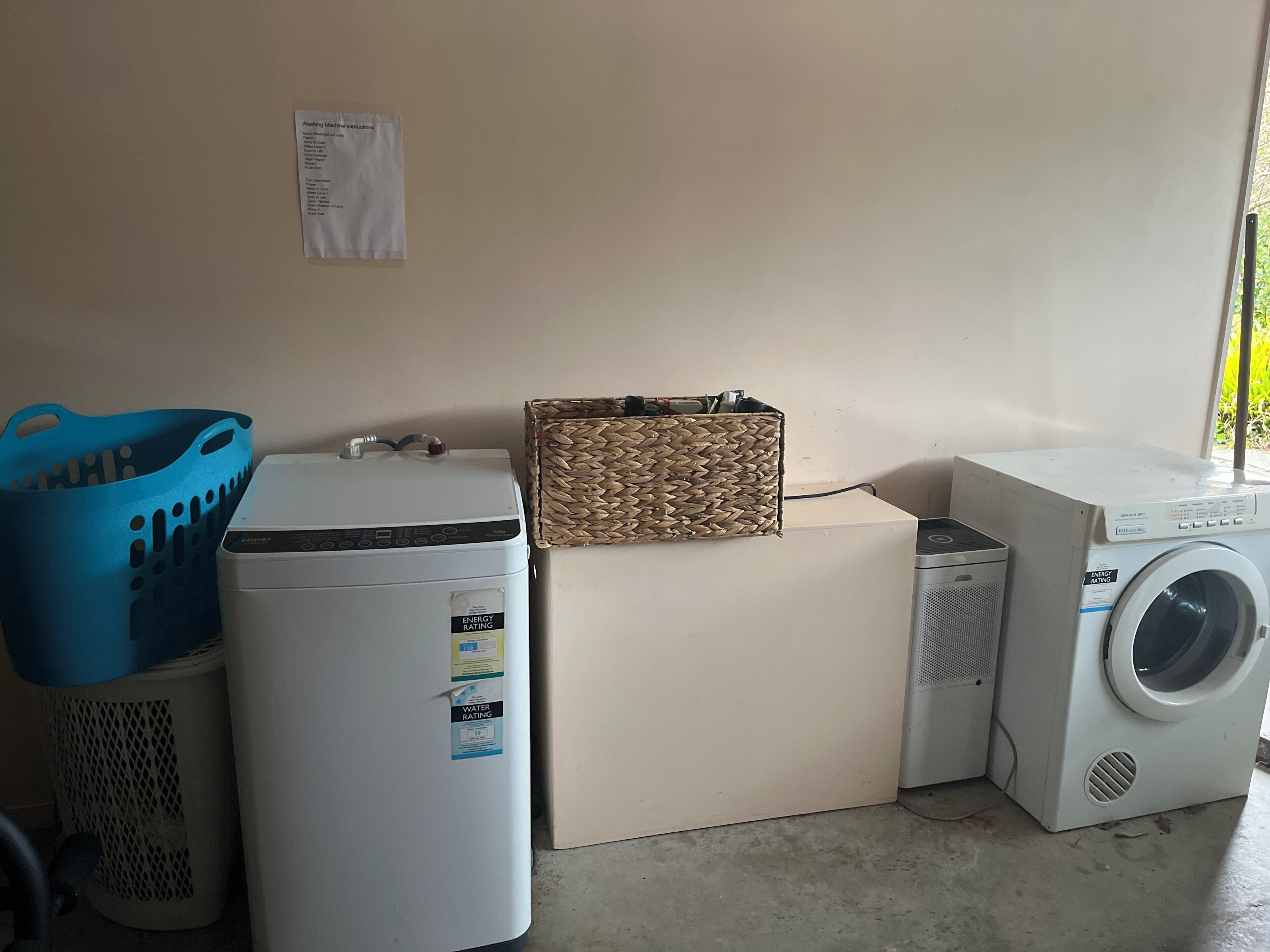 Un espace buanderie comprenant un lave-linge, un sèche-linge, un chauffe-eau et un panier à linge.