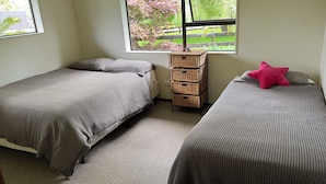 Une chambre avec deux lits, une petite commode en bois et une fenêtre donnant sur un paysage verdoyant.
