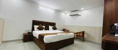 Une chambre d’hôtel avec un grand lit, un bureau, une chaise et un appareil de climatisation fixé au mur.