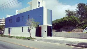 Un edificio moderno con fachada azul, un pequeño árbol en la parte delantera y un cielo despejado.