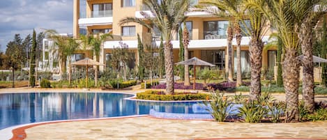 A modern hotel with a large pool, palm trees, and a well-maintained garden.