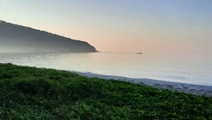 A coastal landscape with a calm sea, a distant boat, and a grassy foreground. - Kampu Nature Pool Villa Rayong (Rayong)
