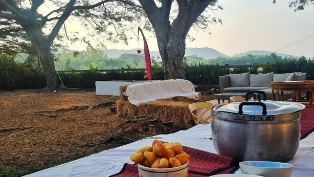An outdoor dining setup with a table, pots, bowls, and a basket of food, set against a backdrop of trees and hills. - Kampu Nature Pool Villa Rayong (Rayong)