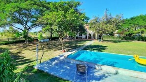 A swimming pool with a yellow float, surrounded by trees and a building in the background. - Kampu Nature Pool Villa Rayong (Rayong)