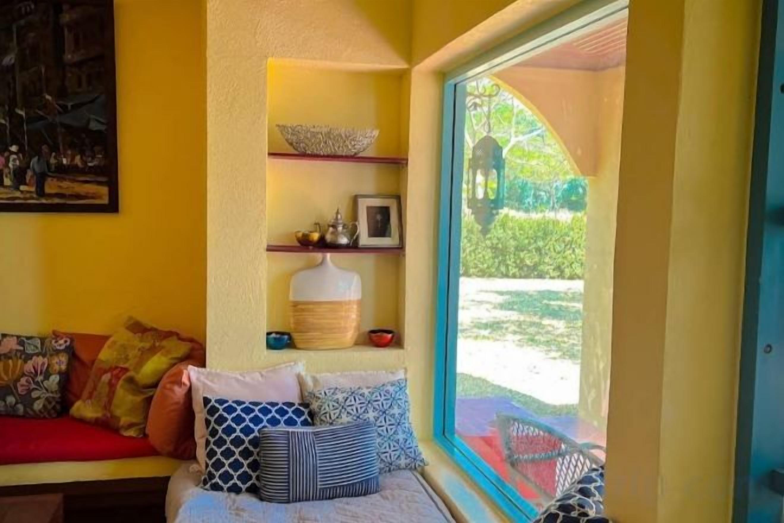 Una habitación con cama, ventana, repisa con adornos y un cuadro en la pared.
