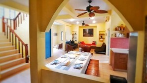 A dining area with a table set for four, a ceiling fan, and a kitchen area with cabinets and a countertop. - Kampu Nature Pool Villa Rayong (Rayong)