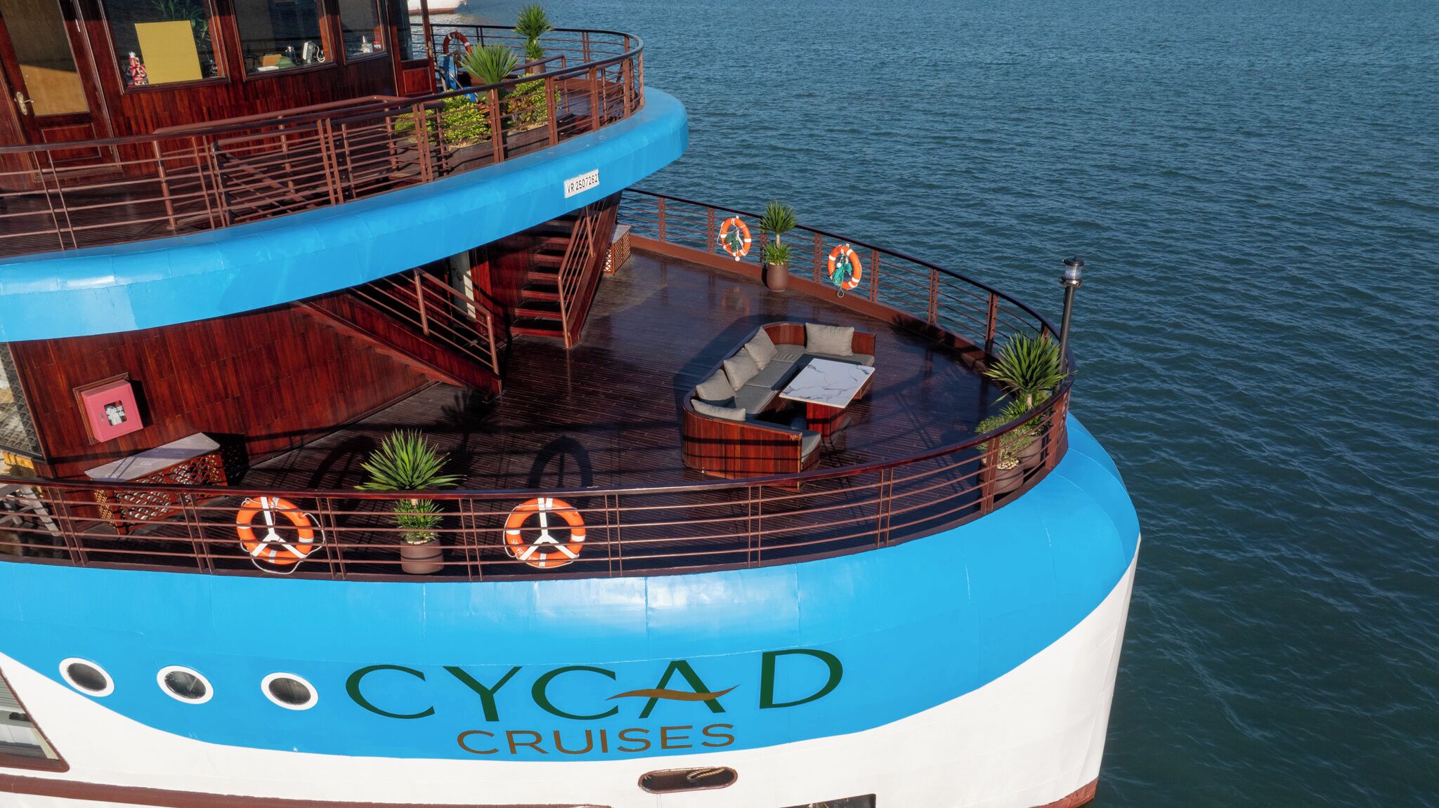 A cruise ship with a blue and white hull, a deck with a seating area, and lifebuoys.