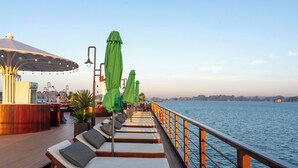 A deck with sun loungers, umbrellas, and a bar area overlooking a body of water. - Cycad Cruise (Bai Chay)