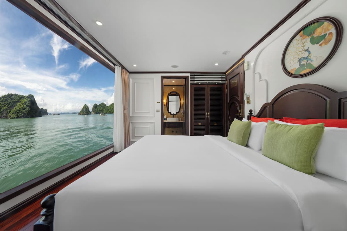 A bedroom with a large bed, a view of the water, and a door leading to a bathroom.