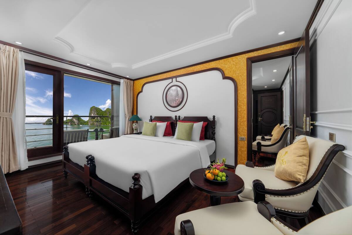 A hotel room with a large bed, a sitting area with a chair and a small table, and a view of the sea through a large window.