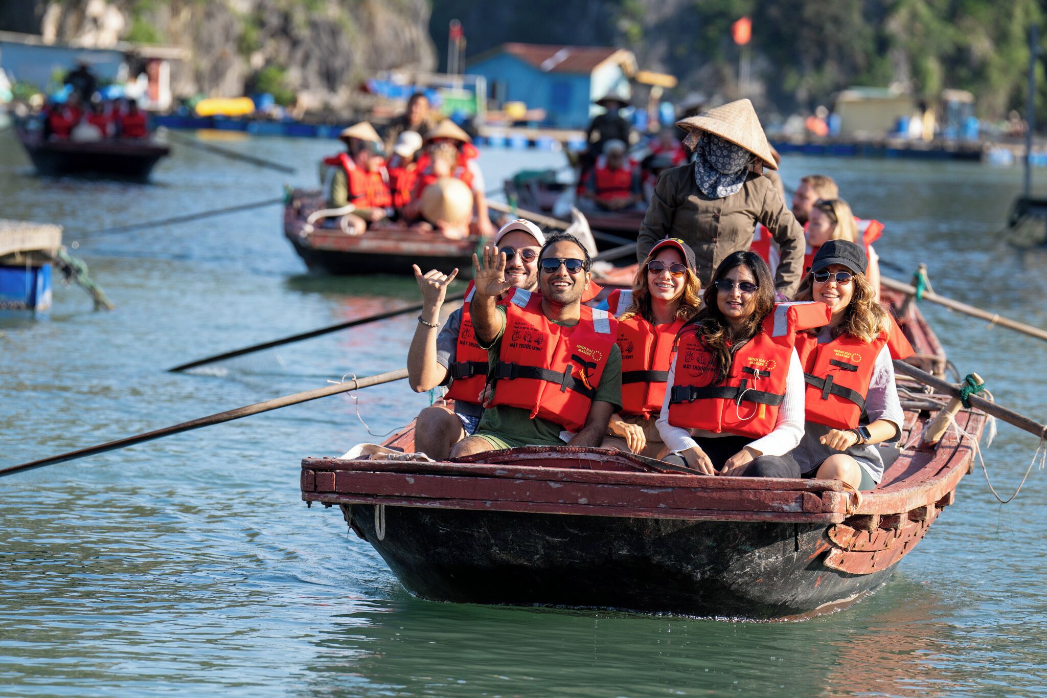 A group of people in a traditional boat, wearing life jackets, on a calm body of water.