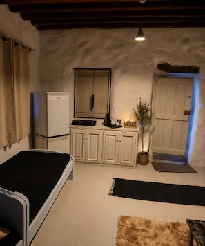 A bedroom with a bed, a small table, a dresser, a mirror, a door, and a window.