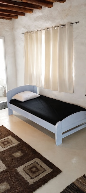 A single bed with a white headboard and footboard, a black mattress, and a brown and white patterned rug.