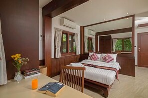 A bedroom with a bed, a table with a book and a glass of orange juice, a chair, and a window with curtains. - Nakawanna Villa (Phuket)