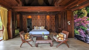 Ein geräumiges Zimmer mit einem großen Bett, zwei Holzstühlen, einem kleinen Tisch und einer Wand mit einem dekorativen Wasserfall.