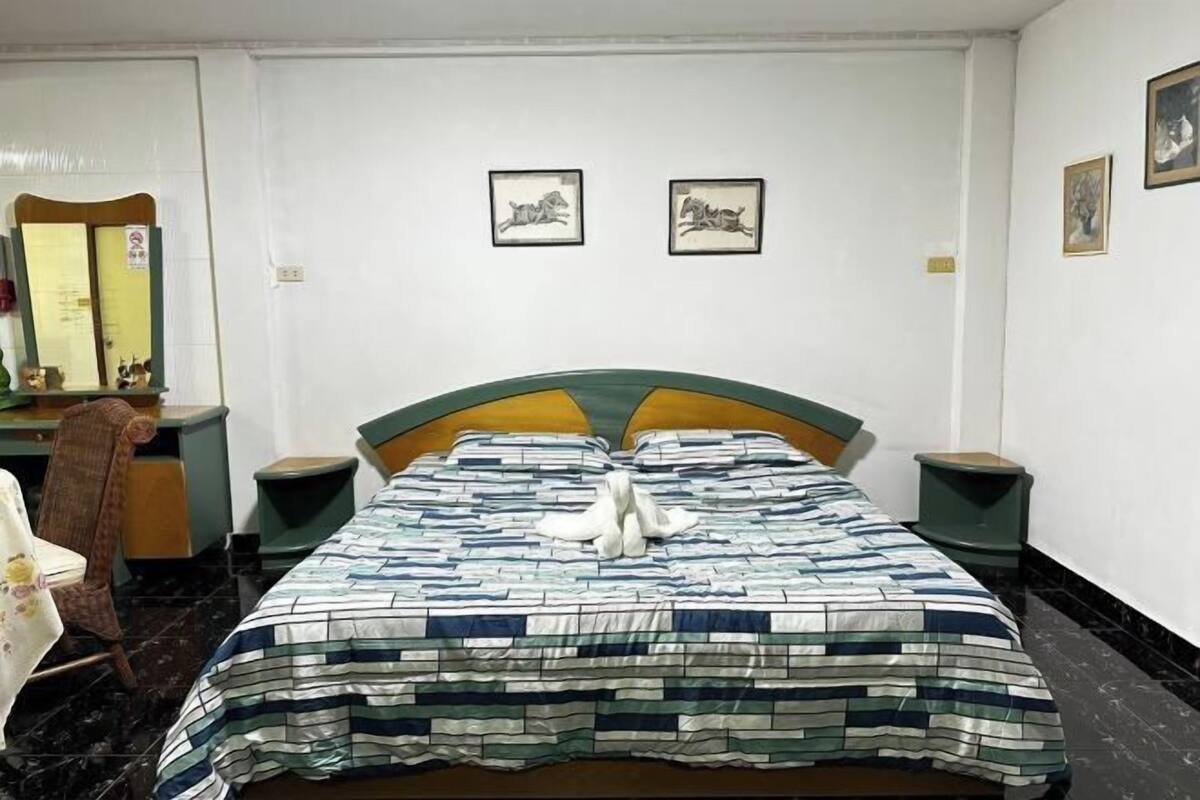 A bedroom with a bed, a chair, a desk, and a mirror. There are two framed pictures on the wall.