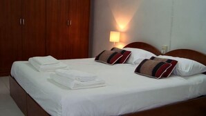 Un letto rifatto con cuscini, un armadio in legno e una lampada a parete.