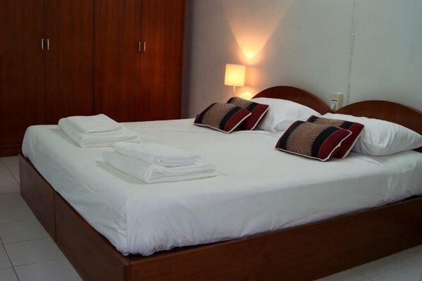 Una cama bien hecha con almohadas, un armario de madera y una lámpara fijada a la pared.