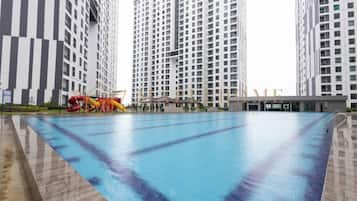 Una piscina amb tobogan i zona de jocs infantils, envoltada d'edificis residencials alts.