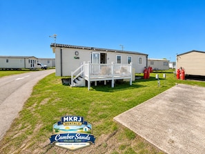 A mobile home with a porch and steps, located in a grassy area with a clear sky.