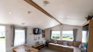 Un espacio habitable compacto con sofá, televisor, reloj y ventana con vista a una zona residencial.