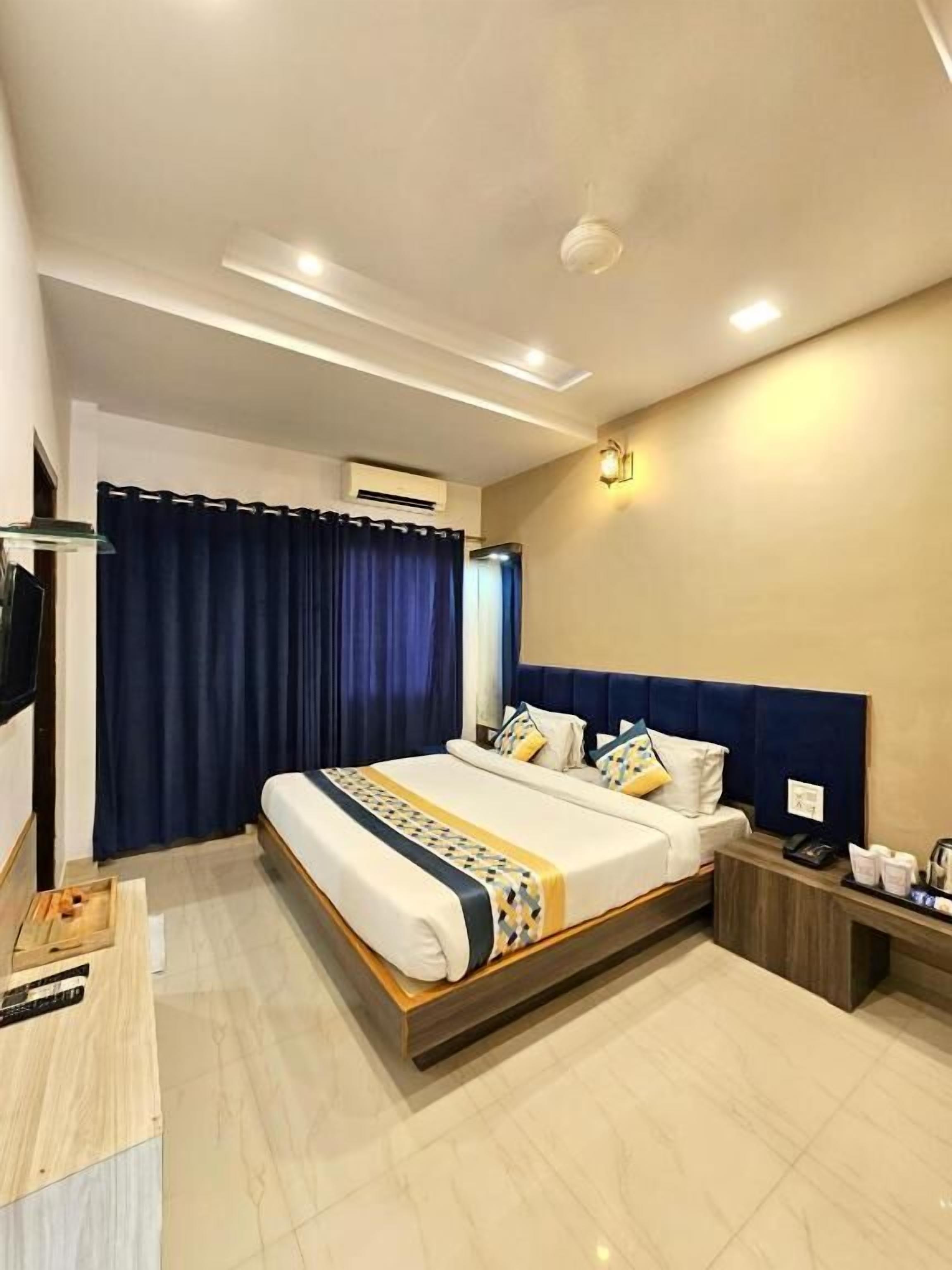 A modern hotel room with a large bed, a bedside table with a lamp, and an air conditioning unit on the wall.