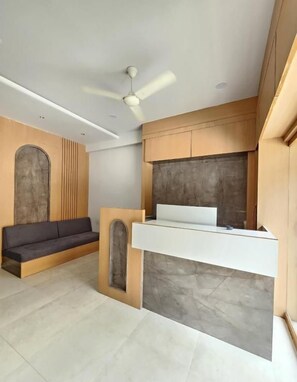 Une pièce moderne et minimaliste, dotée d’un bureau intégré, d’un canapé foncé et d’un ventilateur de plafond.